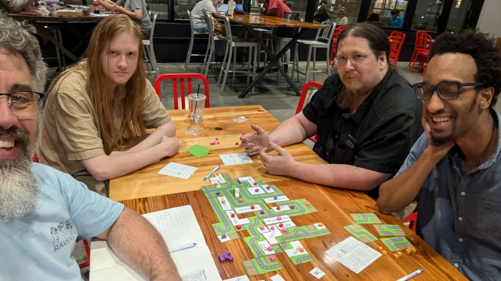 Image of four people sitting around a table with the game finished. Everyone is smiling and looking like they had fun.