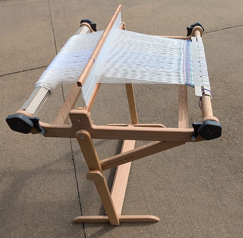 Rigid heddle loom on a stand. It is warped and ready to begin weaving.